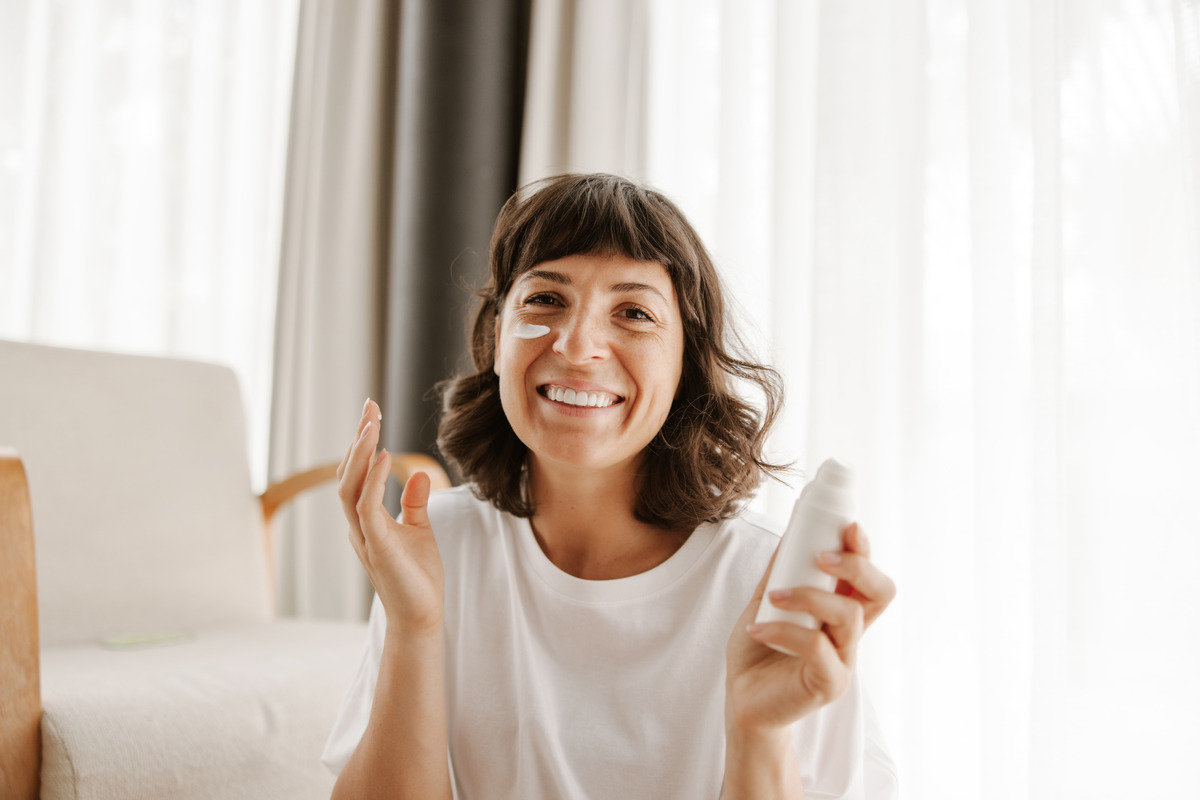 close-up-view-smiling-woman-skin-cream-looking-camera-with-bottle-product-home